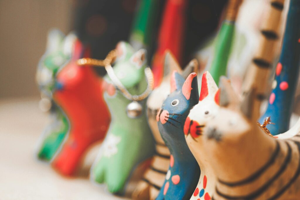 Colorful wooden cat figurines in various patterns and colors, arranged in a row, with a shallow depth of field creating a blurred background effect.